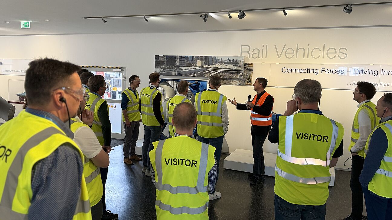 Fachtagung Technische Sauberkeit 2026 - werksführung bei Voith. Teilnehmer werden von hinten Richtung Sprecher fotografiert und tragen Visitor Westen in gelb