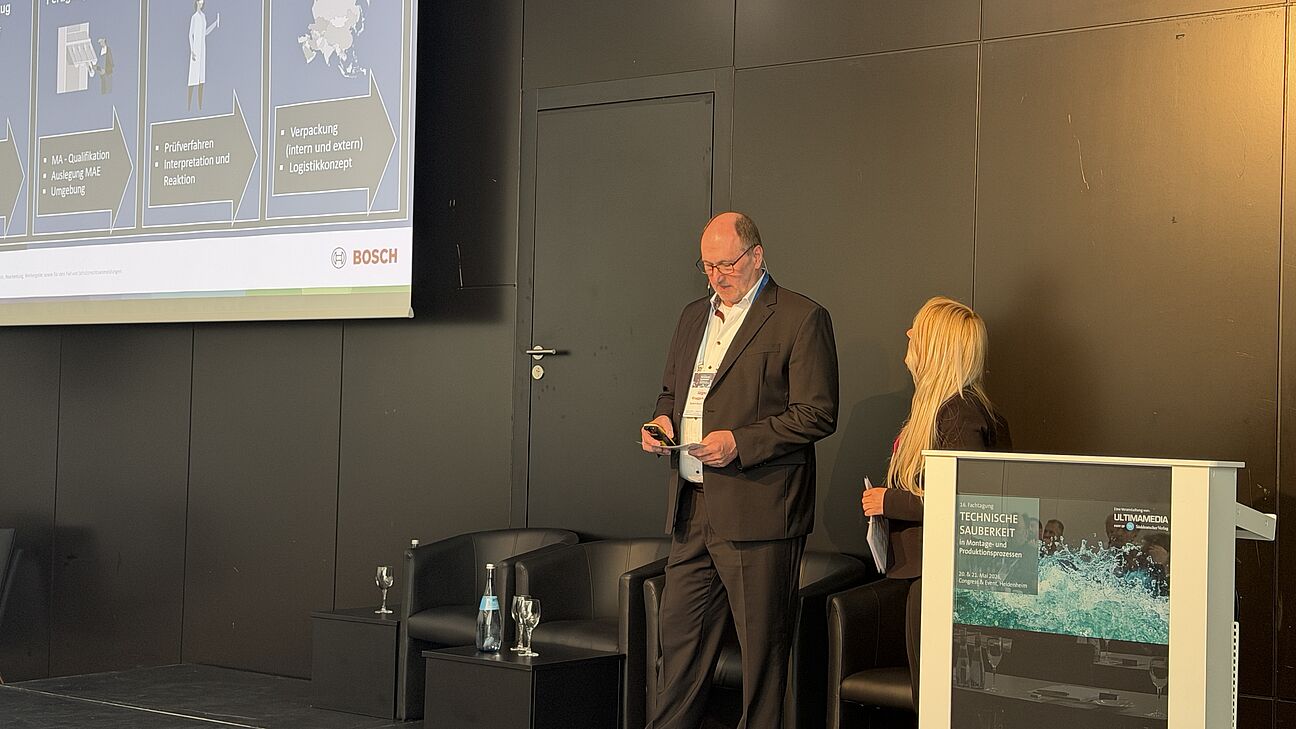 Fachtagung Technische Sauberkeit 2026 - Moderator und Sabrina Appel auf der Bühne hält seinen Vortrag mit einer Präsentation die er den Teilnehmern zeigt
