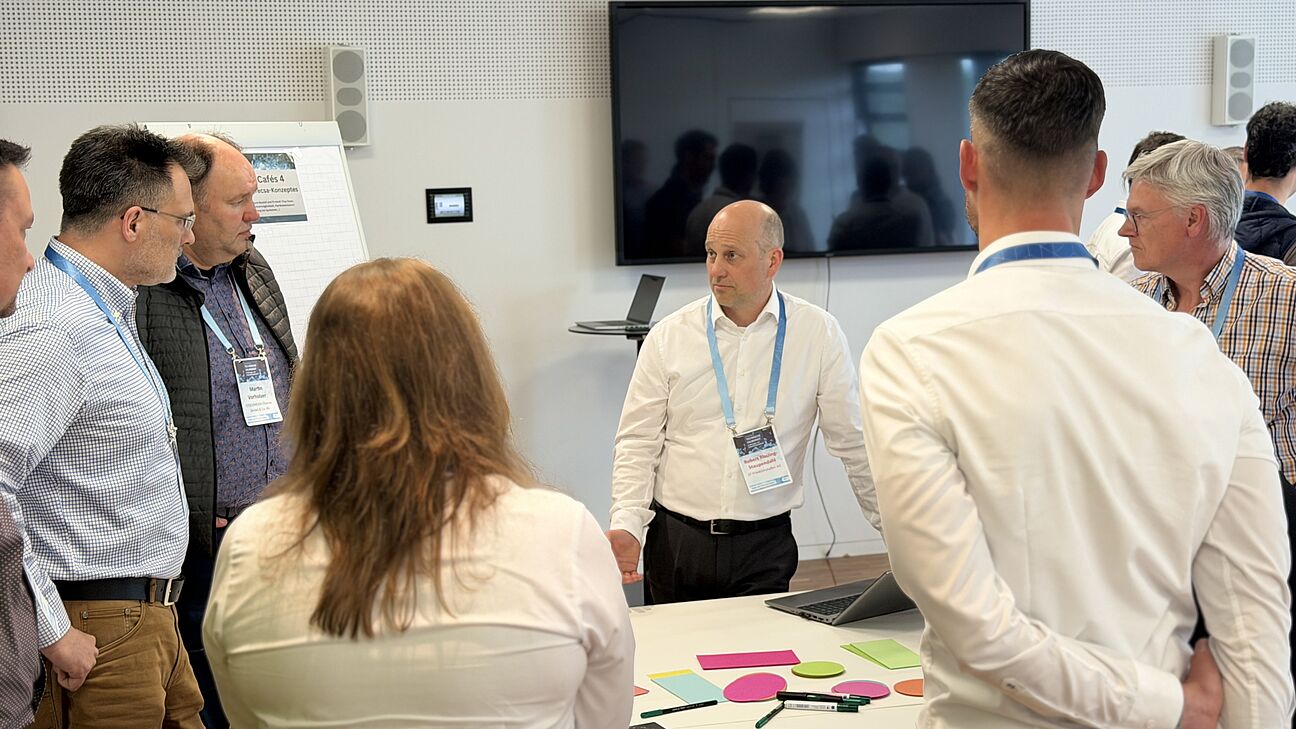 Fachtagung Technische Sauberkeit 2026 - Workshop 4 Teilnehmer stehen um einen Tisch und diskutieren über Technische Sauberkeit