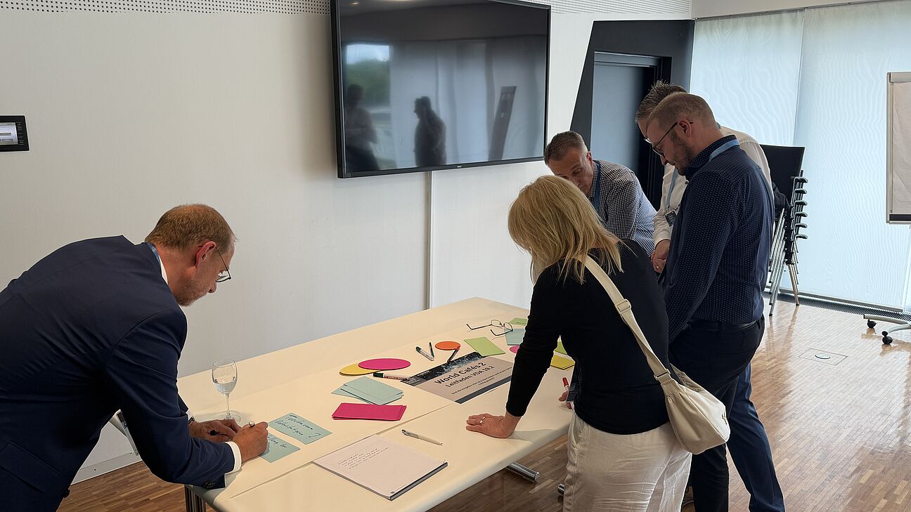Fachtagung Technische Sauberkeit 2026 - Workshop 4 Teilnehmer stehen um einen Tisch und diskutieren über Technische Sauberkeit